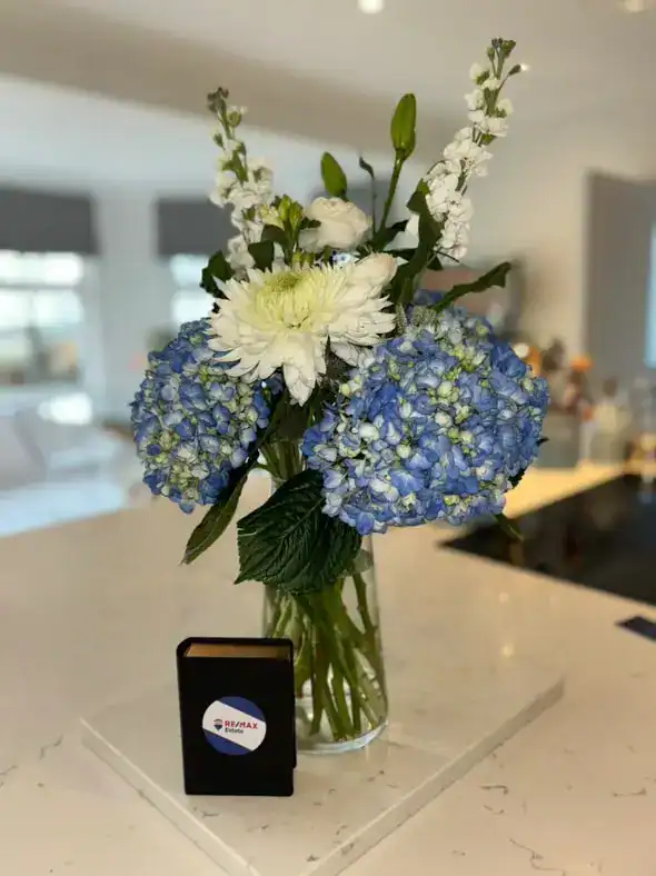 An elegant bouquet of blue hydrangeas, white chrysanthemums, and delicate white flowers in a clear g.