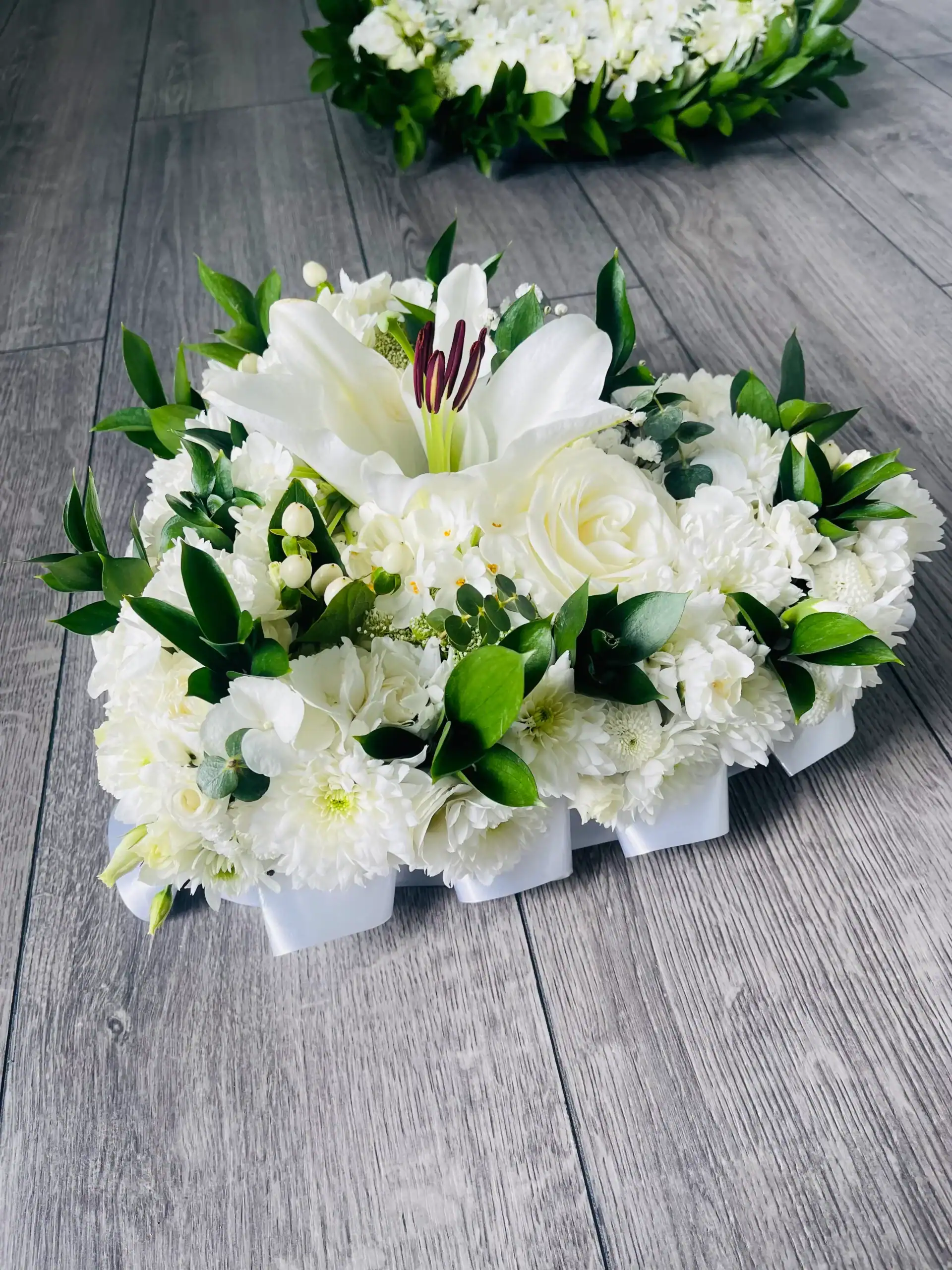 Elegant white floral arrangement with lilies, roses, and greenery.
