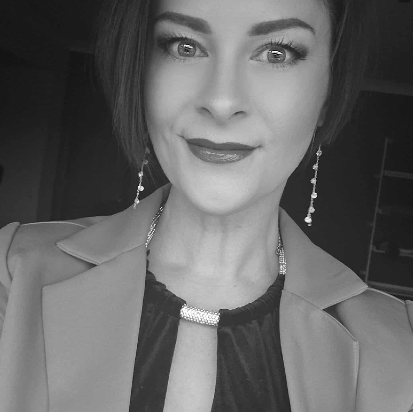 Elegant woman with short hair, wearing jewelry, smiling confidently in a professional portrait.