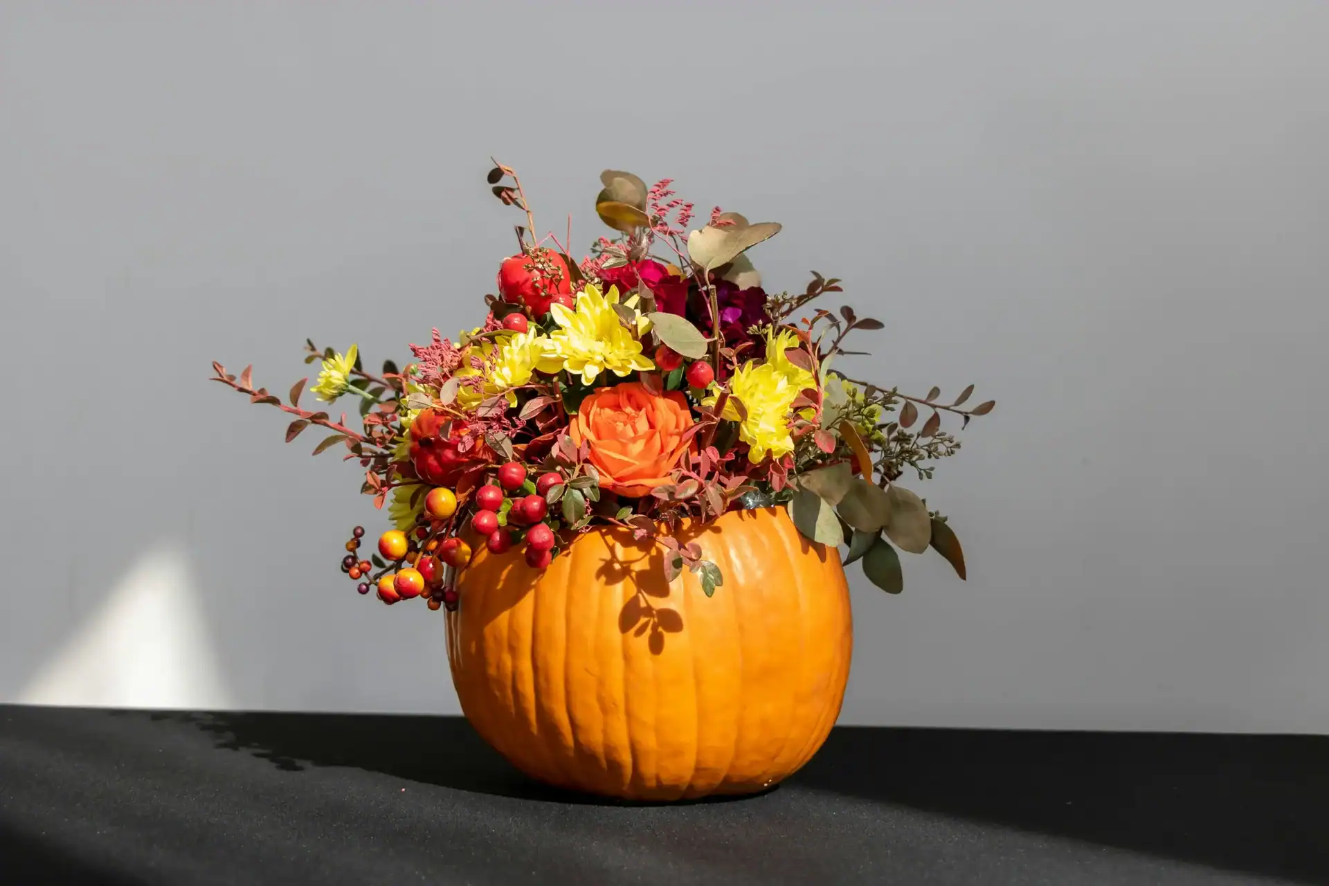 Autumn pumpkin with vibrant flowers and berries in a pumpkin-shaped vase. Perfect for seasonal home.