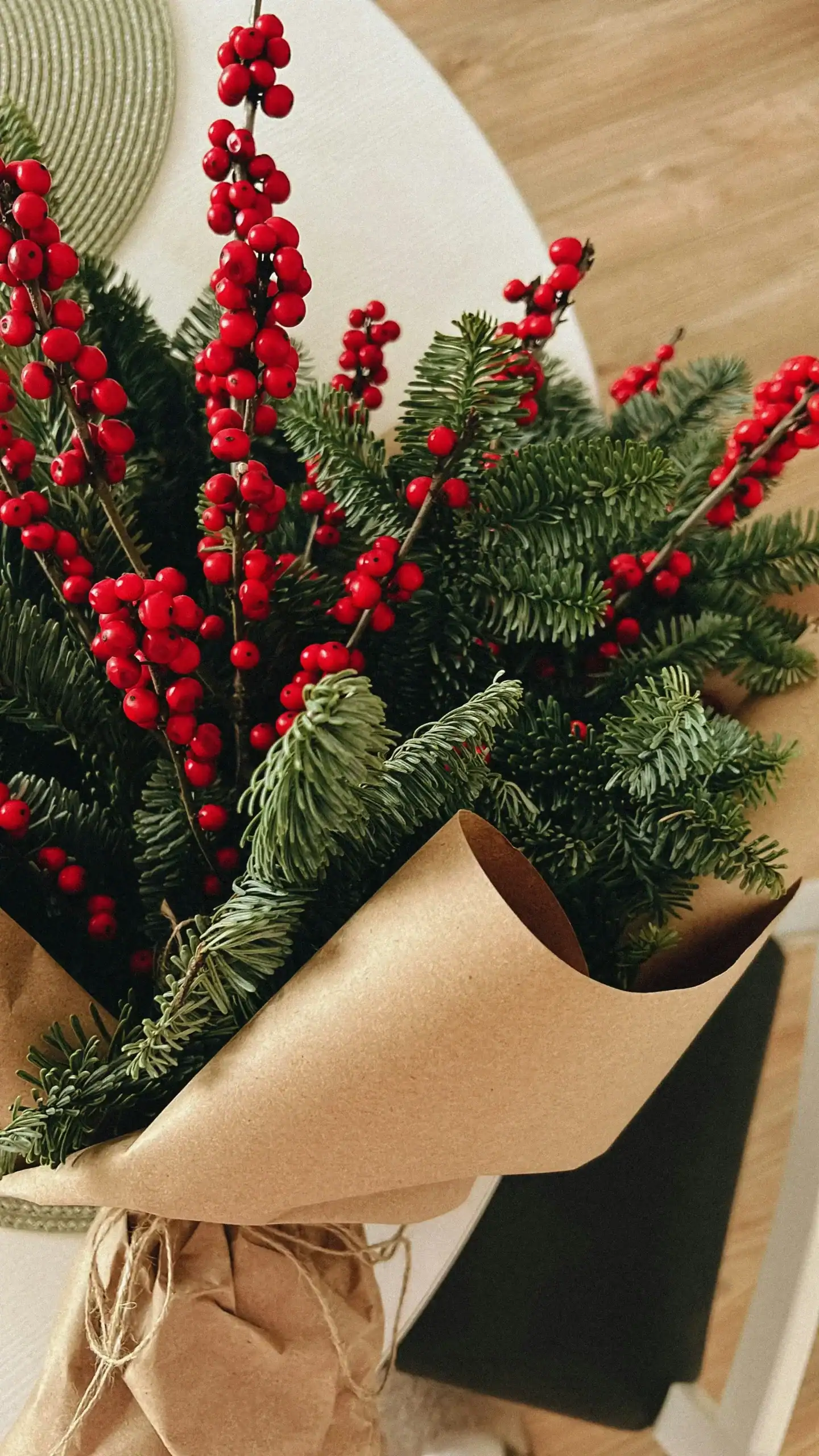 Festive holiday flower arrangement with red berries and pine branches in kraft paper wrapping.