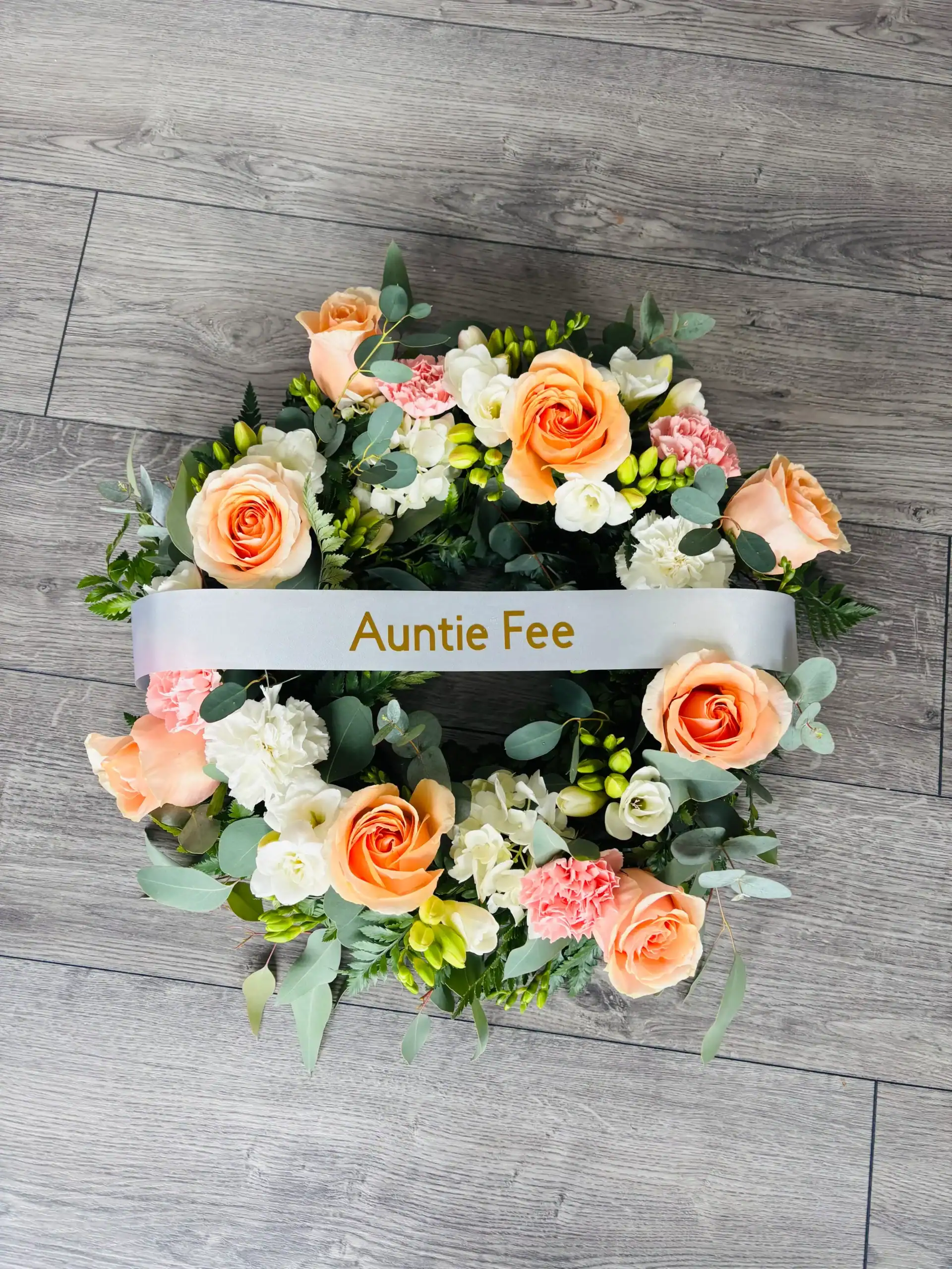 Elegant floral wreath featuring peach roses, white blooms, and greenery for Auntie Fee.